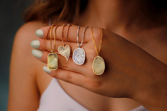 Hand holding five gold necklaces with different pendants against a blurred background