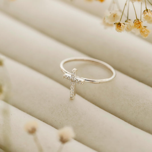 Silver cross ring on a beige surface with dried flowers in the background