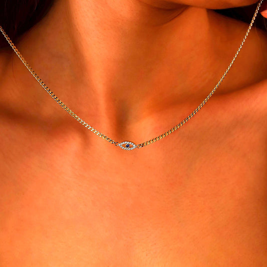 Gold necklace with a blue gemstone on a person's neck against an orange background