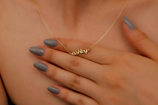 Gold necklace with 'Ashley' pendant on a person's chest with hand