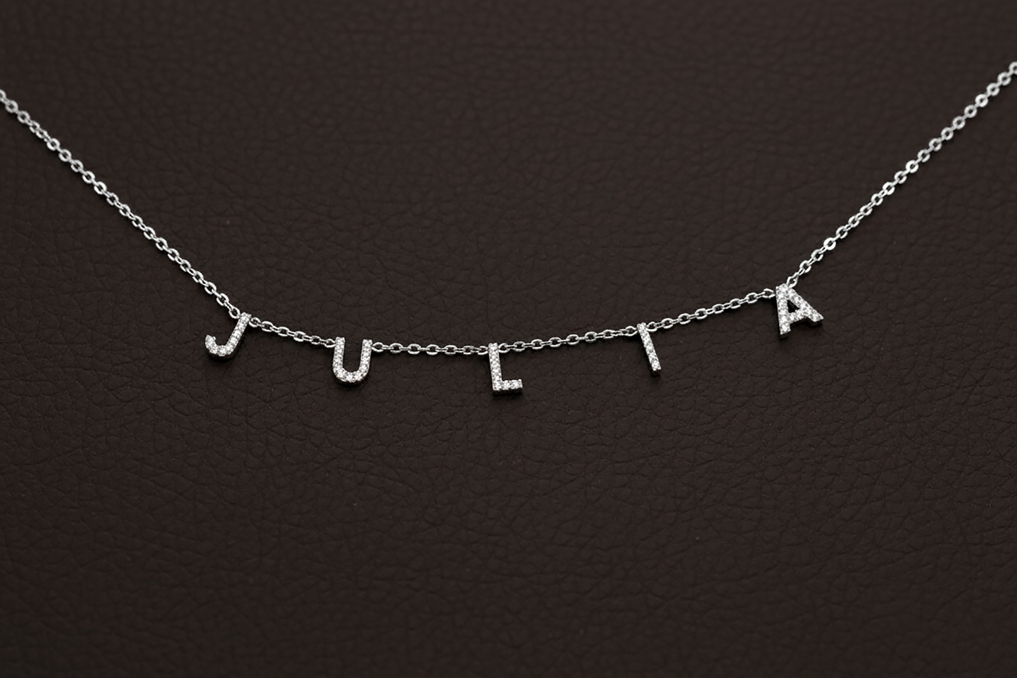 Silver necklace with 'JULIA' letters on a dark background