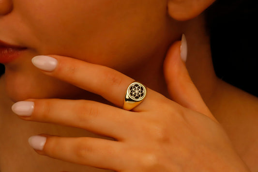 A gold signet ring featuring a geometric "Seed of Life" engraving, shown being worn on a hand and showcased from various angles. A product by SilverGoldandRose.com.