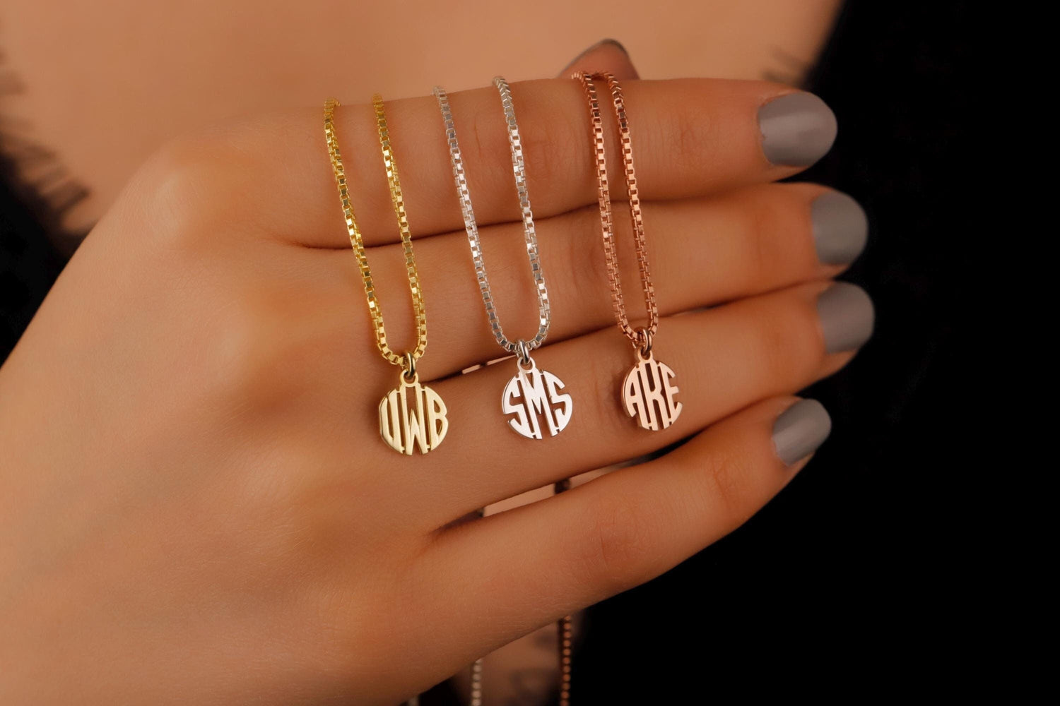 A close-up image of 3 personalized monogram necklaces with a tiny initial pendant on a box chain in Silver Gold and Rose, holding by a person.
