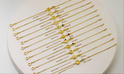 Set of gold flower necklaces and bracelets with birthstone charms on a heart-shaped stand