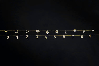 Gold jewelry charms including numbers, animals, and symbols on a black background