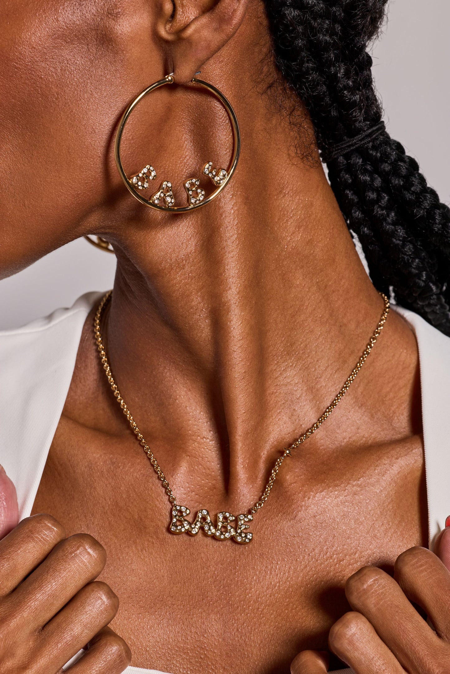 Close-up of a person wearing gold hoop earrings and necklace with 'LOVE' on a neutral background