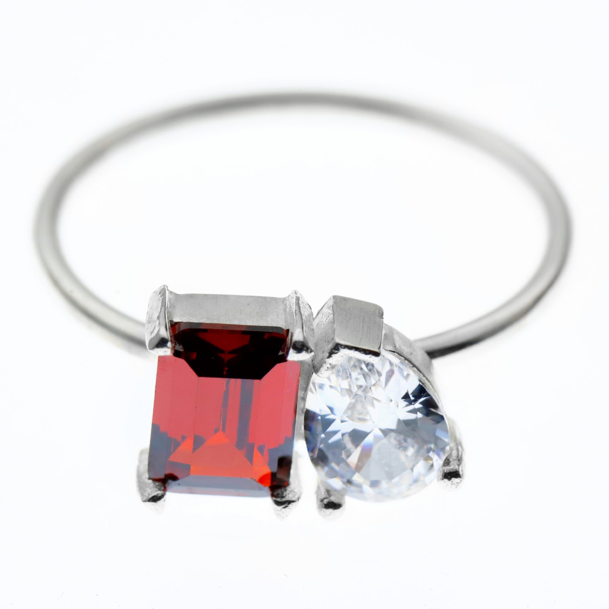 Silver ring with a red square gemstone and clear round gemstone on a white background