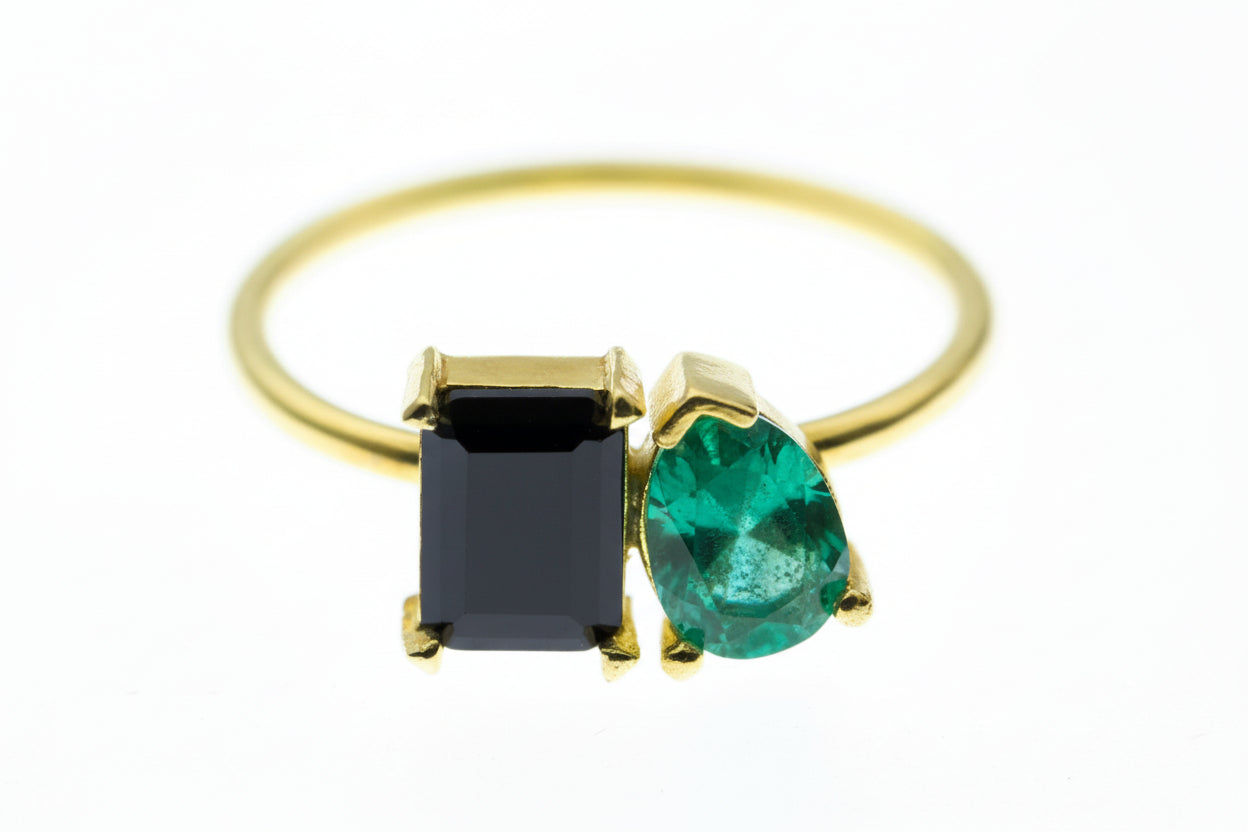Gold ring with a black square gem and blue teardrop gem on a white background