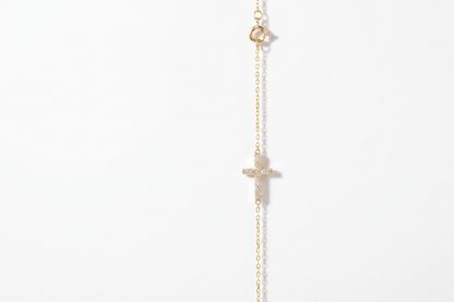 A delicate gold chain necklace featuring a small cross pendant and a tiny round bead at the top, displayed against a solid white background.
