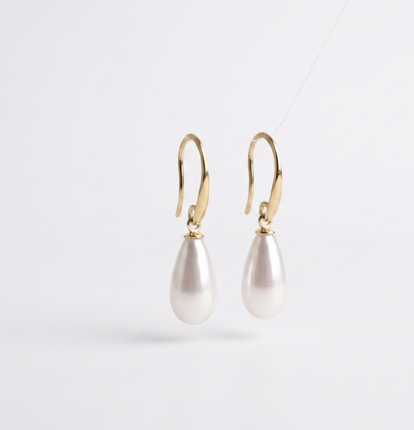 Pearl earrings with gold hooks on a light gray background