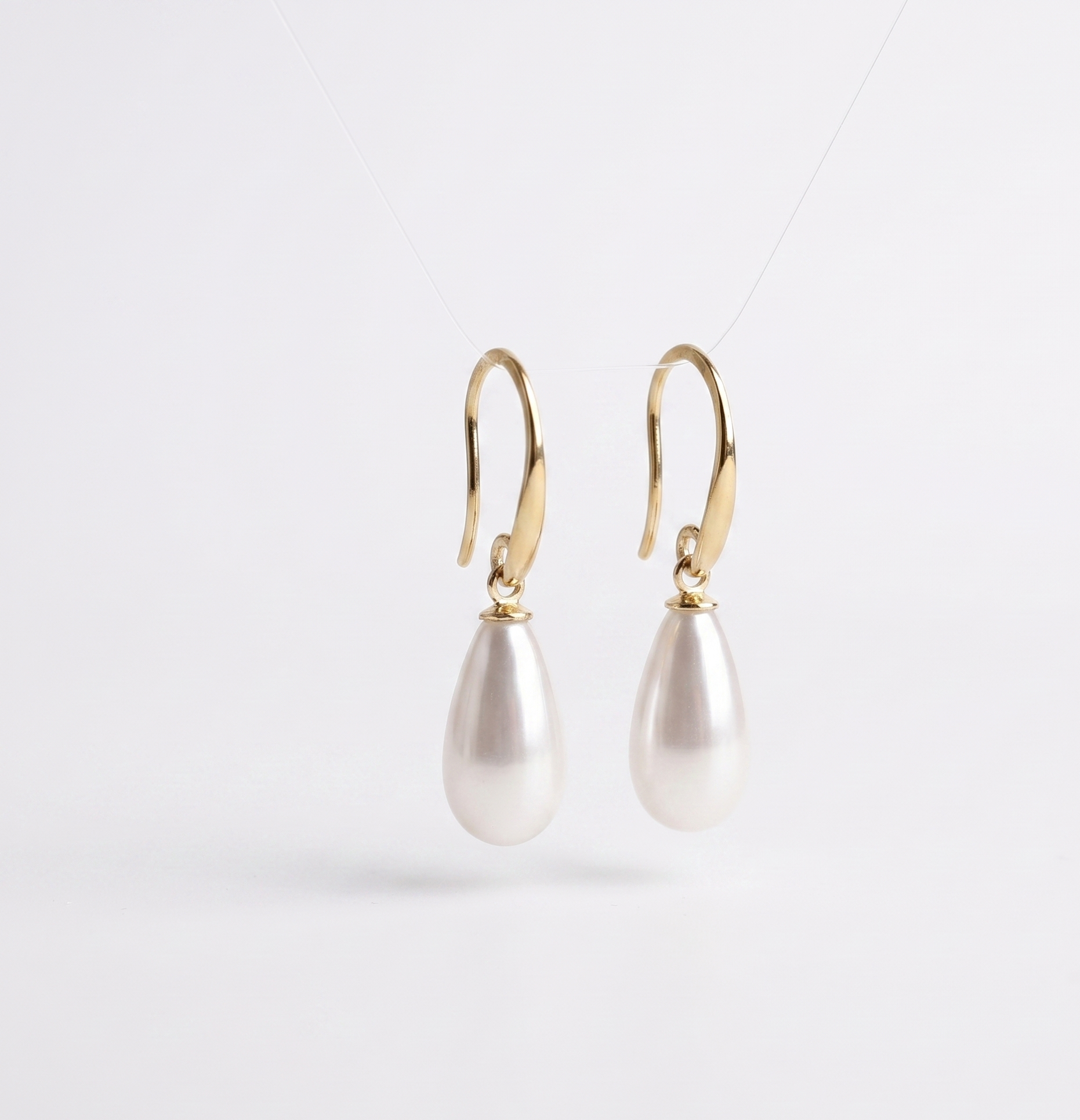 Pearl earrings with gold hooks on a light gray background