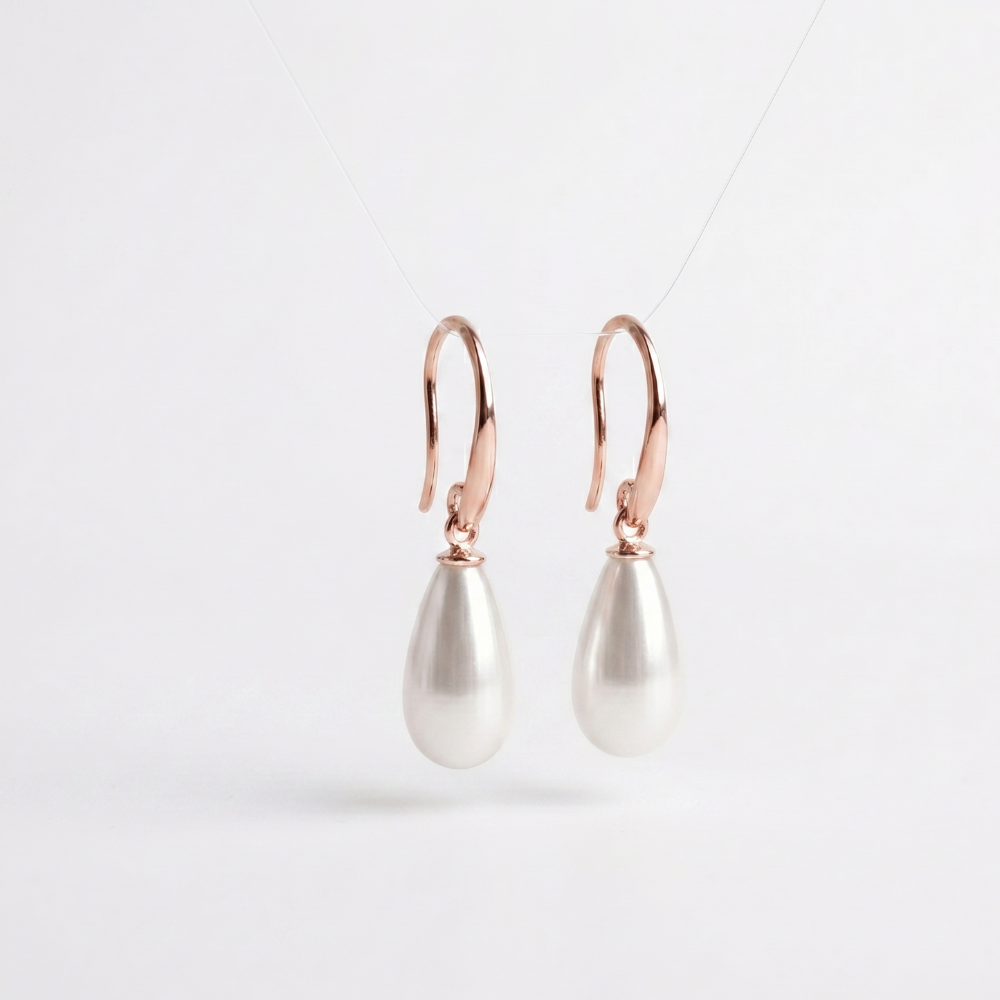 Pearl drop earrings with rose gold hooks on a light gray background