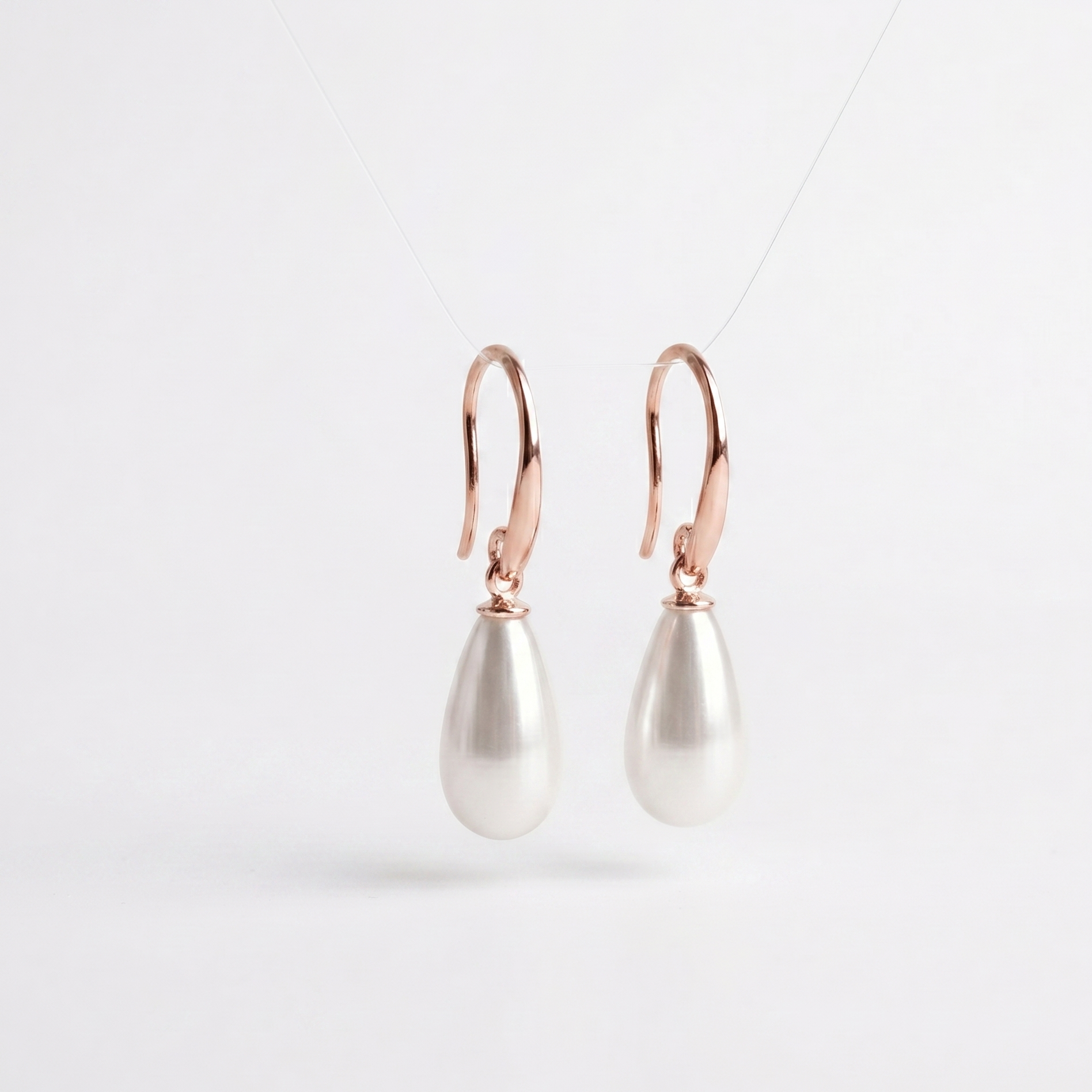 Pearl drop earrings with rose gold hooks on a light gray background
