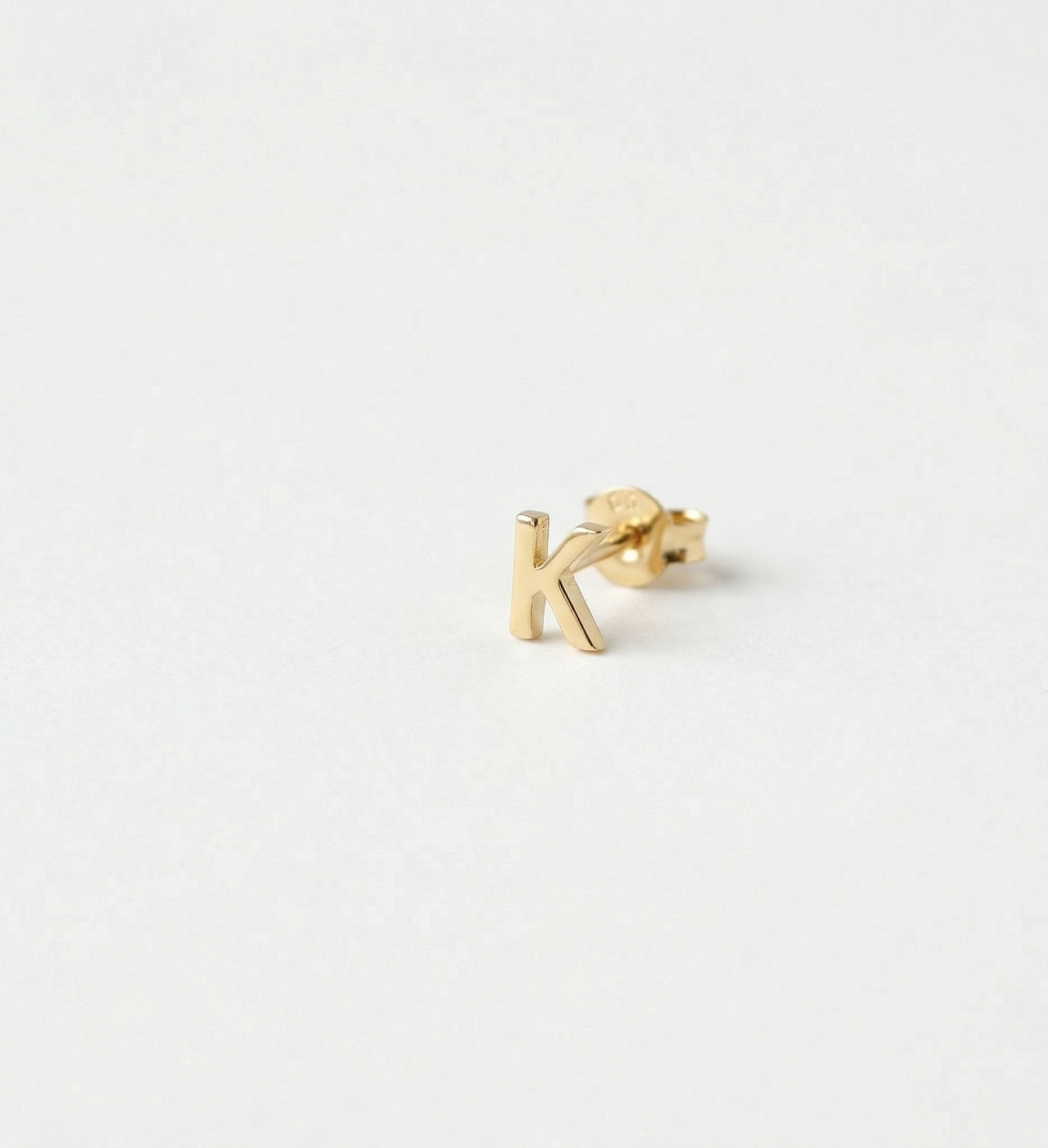 Gold letter 'k' earring on a white background