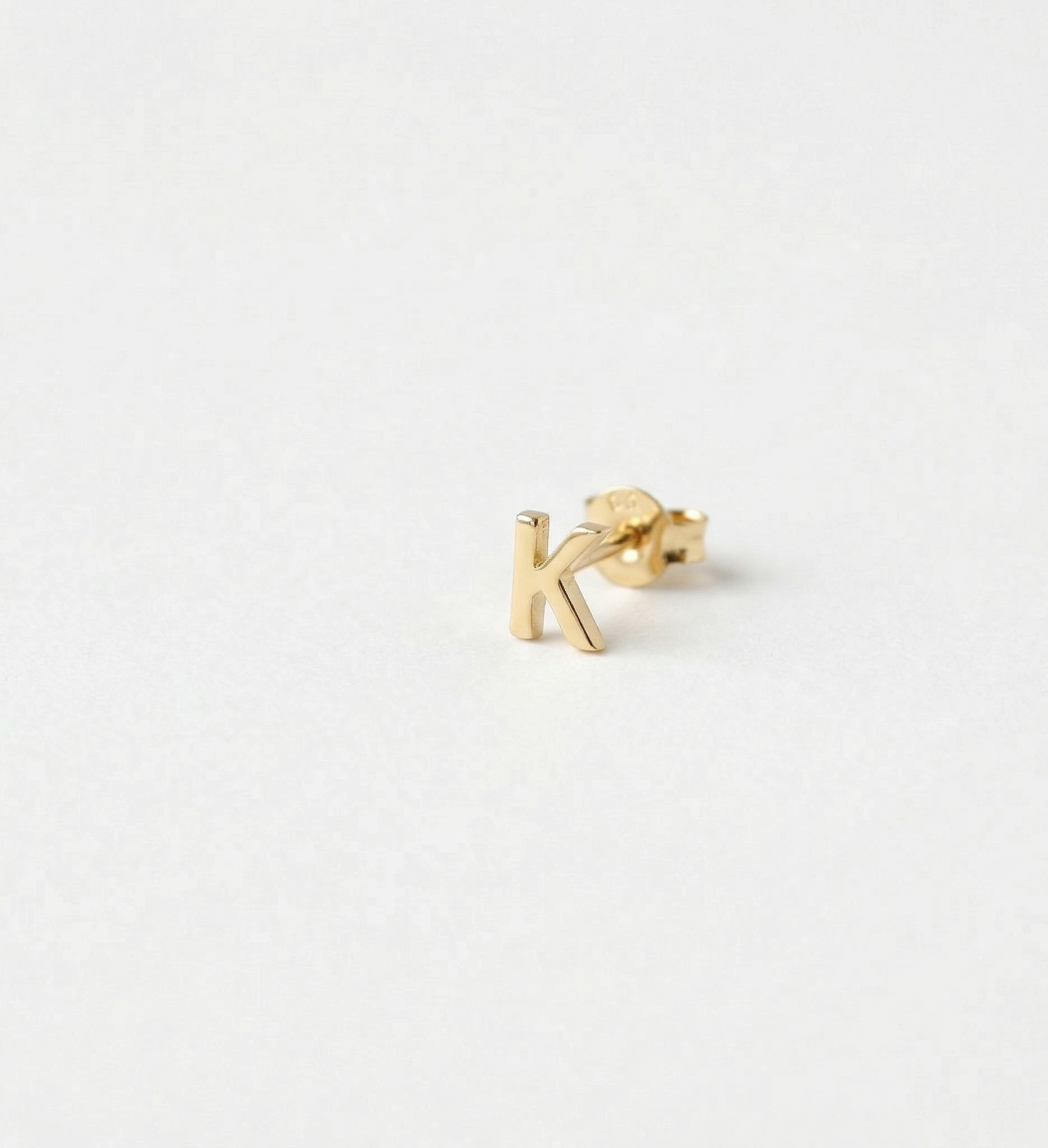 Gold letter 'k' earring on a white background