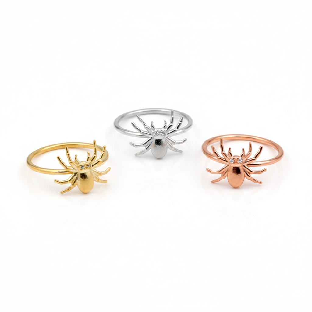 Three spider-shaped rings in gold, silver, and rose gold on a white background