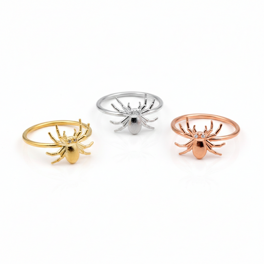 Three spider-shaped rings in gold, silver, and rose gold on a white background