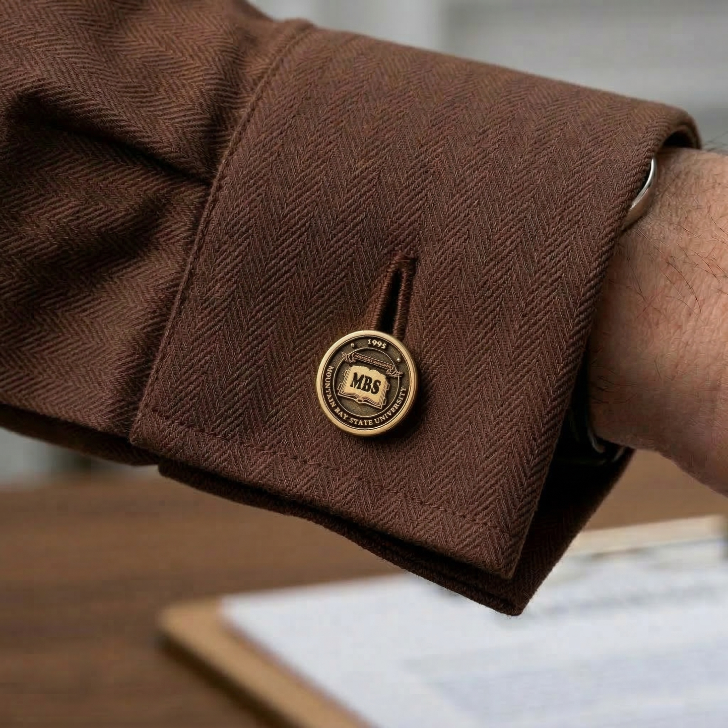 Close-up of a brown herringbone suit cuff with a gold emblem, blurred background