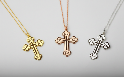 Three cross-shaped pendants on necklaces against a light gray background