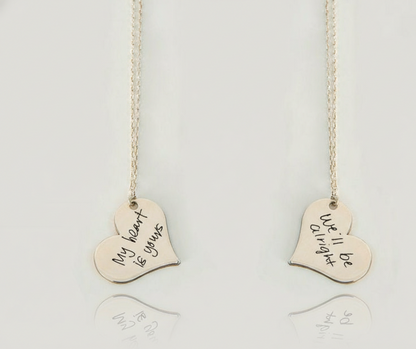 Two heart-shaped pendants on necklaces with engraved text on a light background
