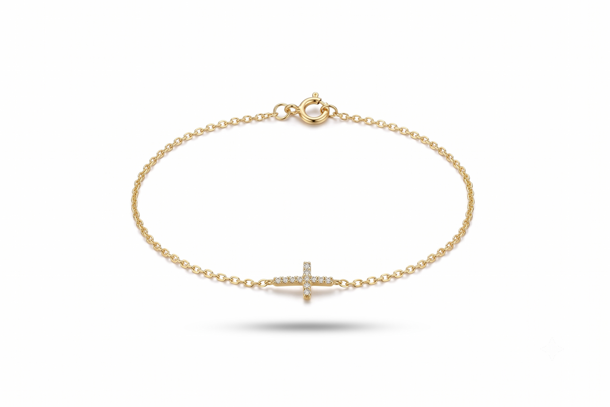 A delicate yellow gold chain bracelet with a small cross charm paved with tiny clear stones, shown on a clean white background.