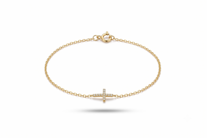 A delicate yellow gold chain bracelet with a small cross charm paved with tiny clear stones, shown on a clean white background.
