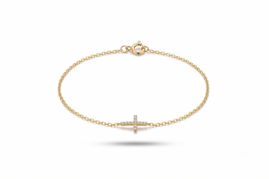 A delicate yellow gold chain bracelet with a small cross charm paved with tiny clear stones, shown on a clean white background.