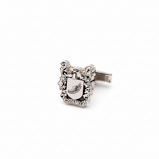 Silver cufflink with crest design on a white background