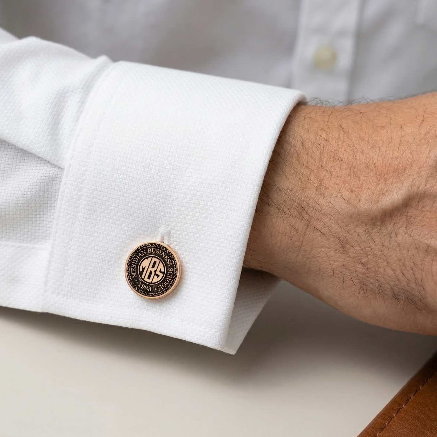 Close-up of a white shirt cuff with a gold and black monogrammed cufflink.