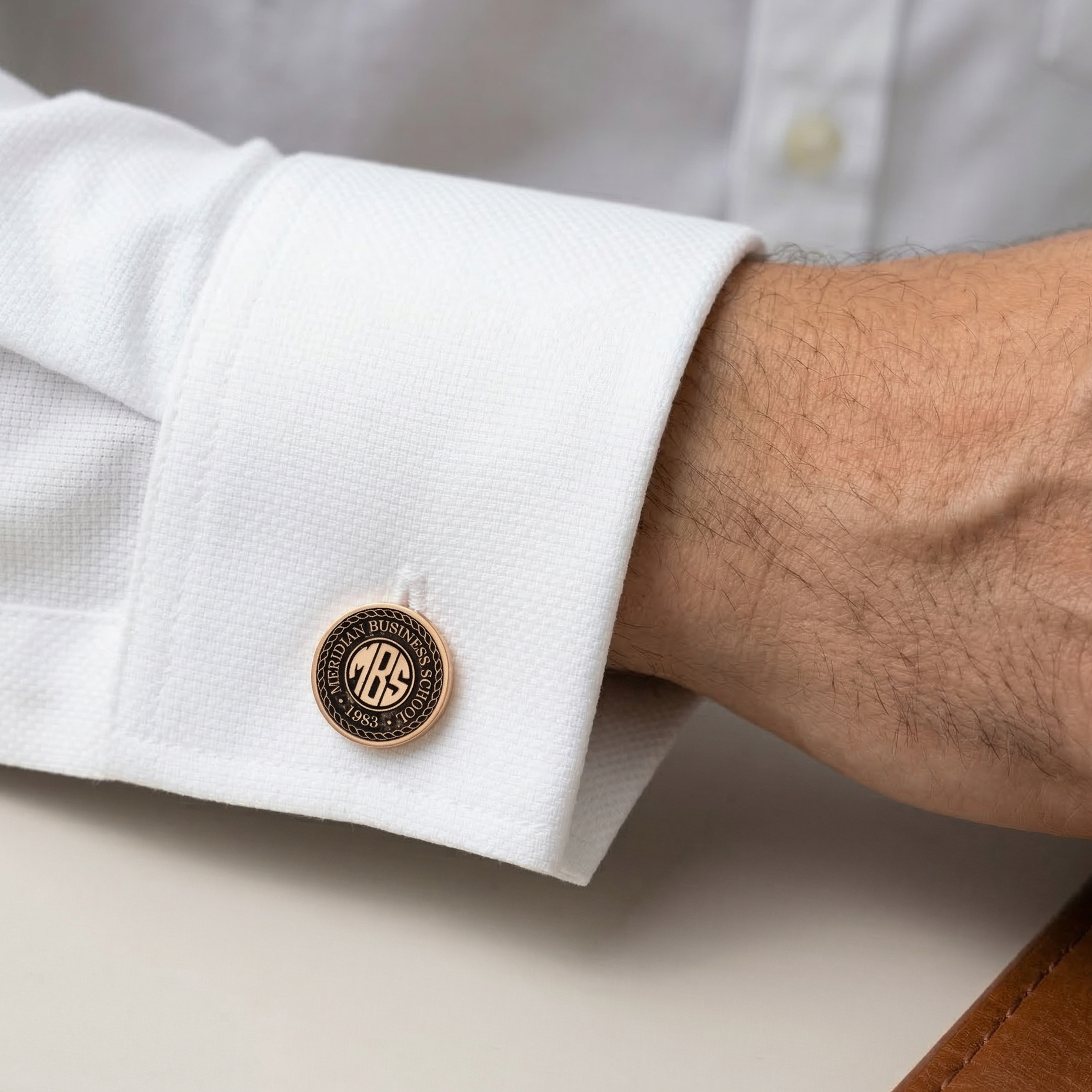 Close-up of a white shirt cuff with a gold and black monogrammed cufflink.