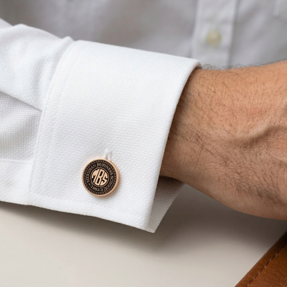 Close-up of a white shirt cuff with a gold and black monogrammed cufflink.