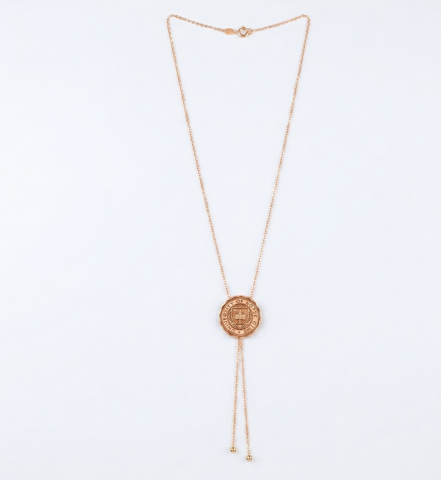 Rose gold necklace with a circular university logo pendant on a light blue background