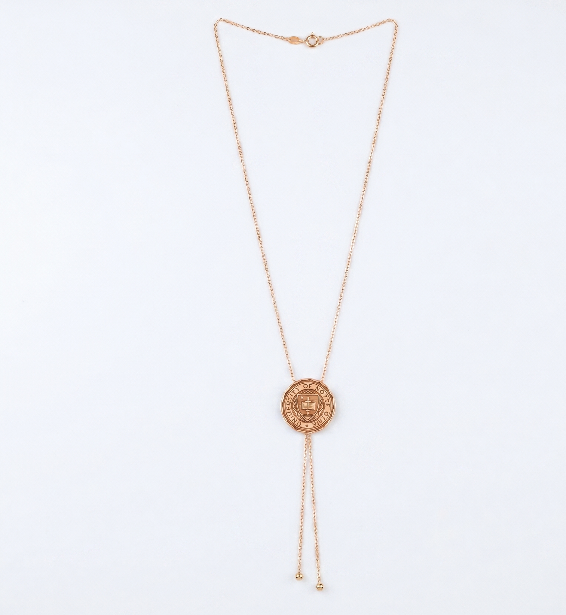 Rose gold necklace with a circular university logo pendant on a light blue background