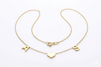 Two gold necklaces with heart and letter pendants on a white background