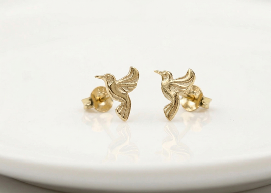 Gold hummingbird earrings on a white surface
