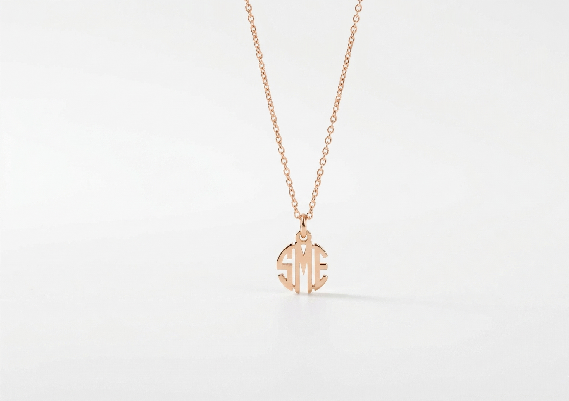 Rose gold necklace with a monogram pendant on a light gray background