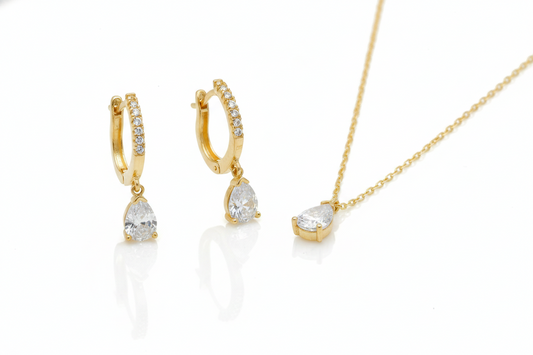 Gold jewelry set featuring diamond dangle earrings with pavé diamonds and a matching teardrop pendant necklace on a delicate chain