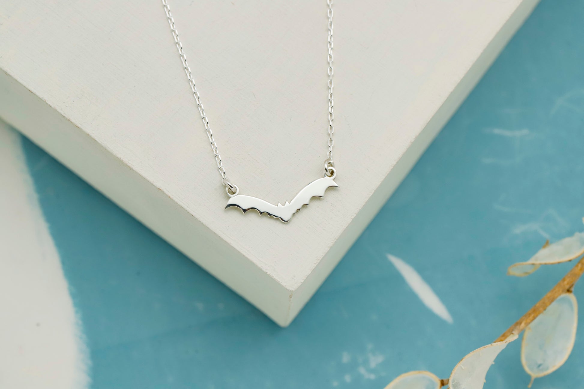Silver necklace with a bat design on a light blue surface