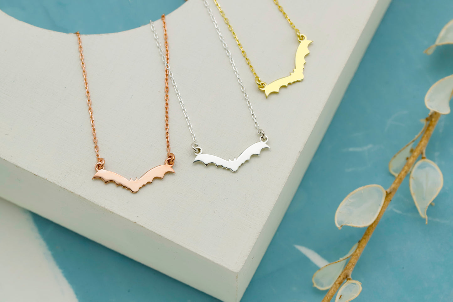 Three necklaces in gold, silver, and rose gold on a white stand with a blue background.