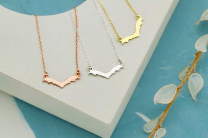 Three necklaces in gold, silver, and rose gold on a white stand with a blue background.