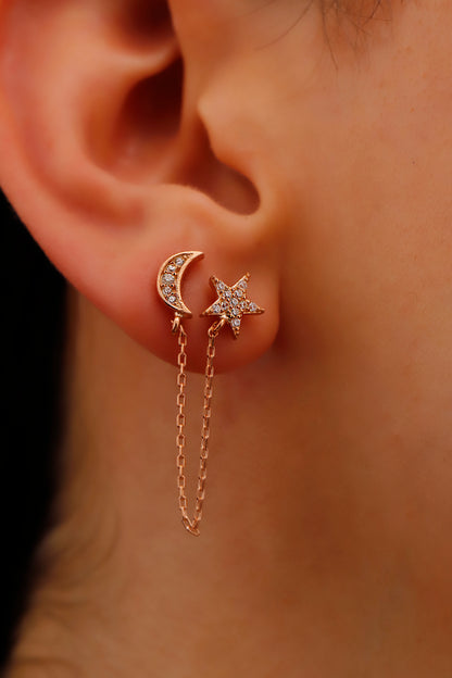 A close-up image of a person wearing ROSE gold-colored pave star and moon earrings with small dangling earrings on the lobes of their ears.