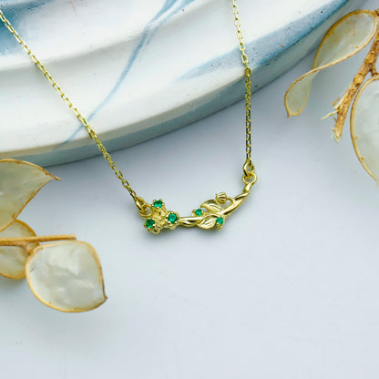 Gold necklace with green gemstones on a white surface with floral elements