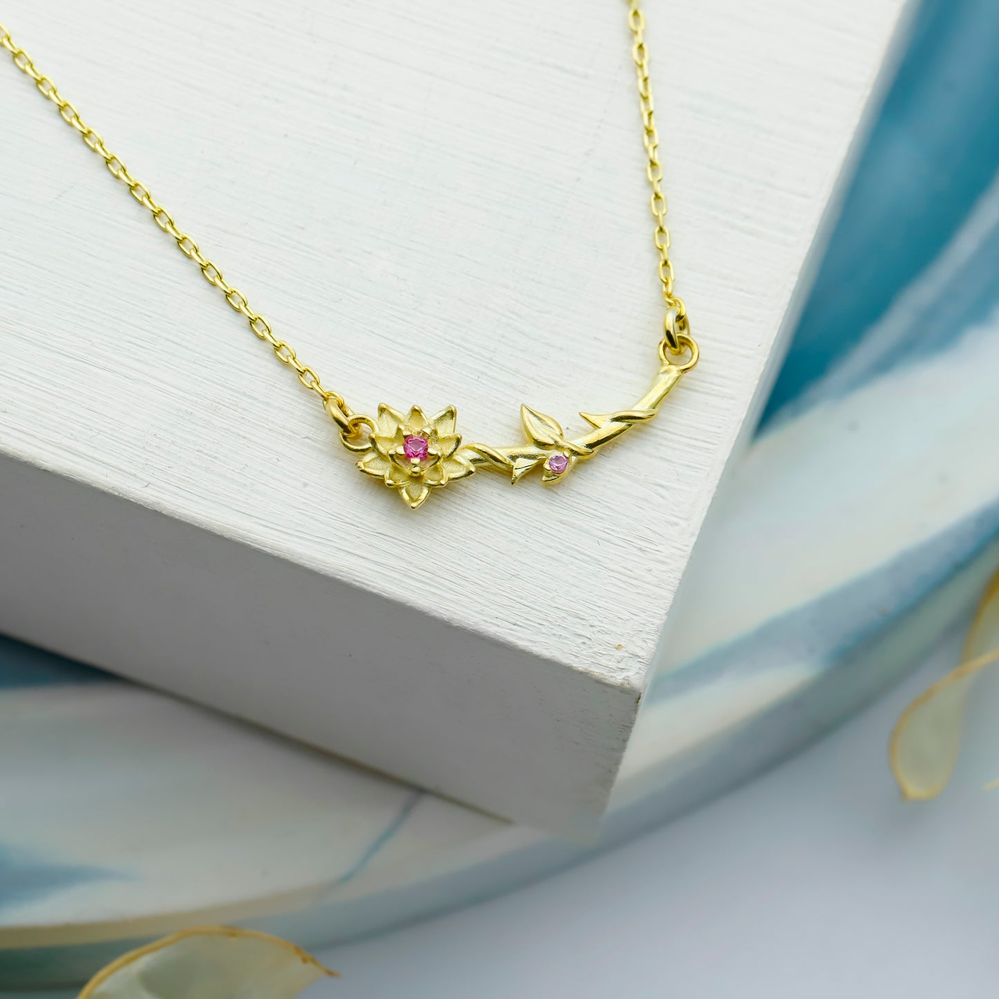 Gold necklace with floral design and pink gemstones on a white surface