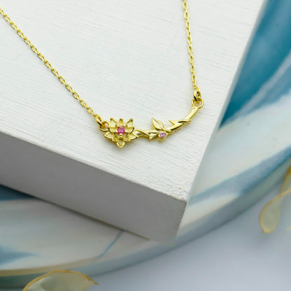 Gold necklace with floral design and pink gemstones on a white surface