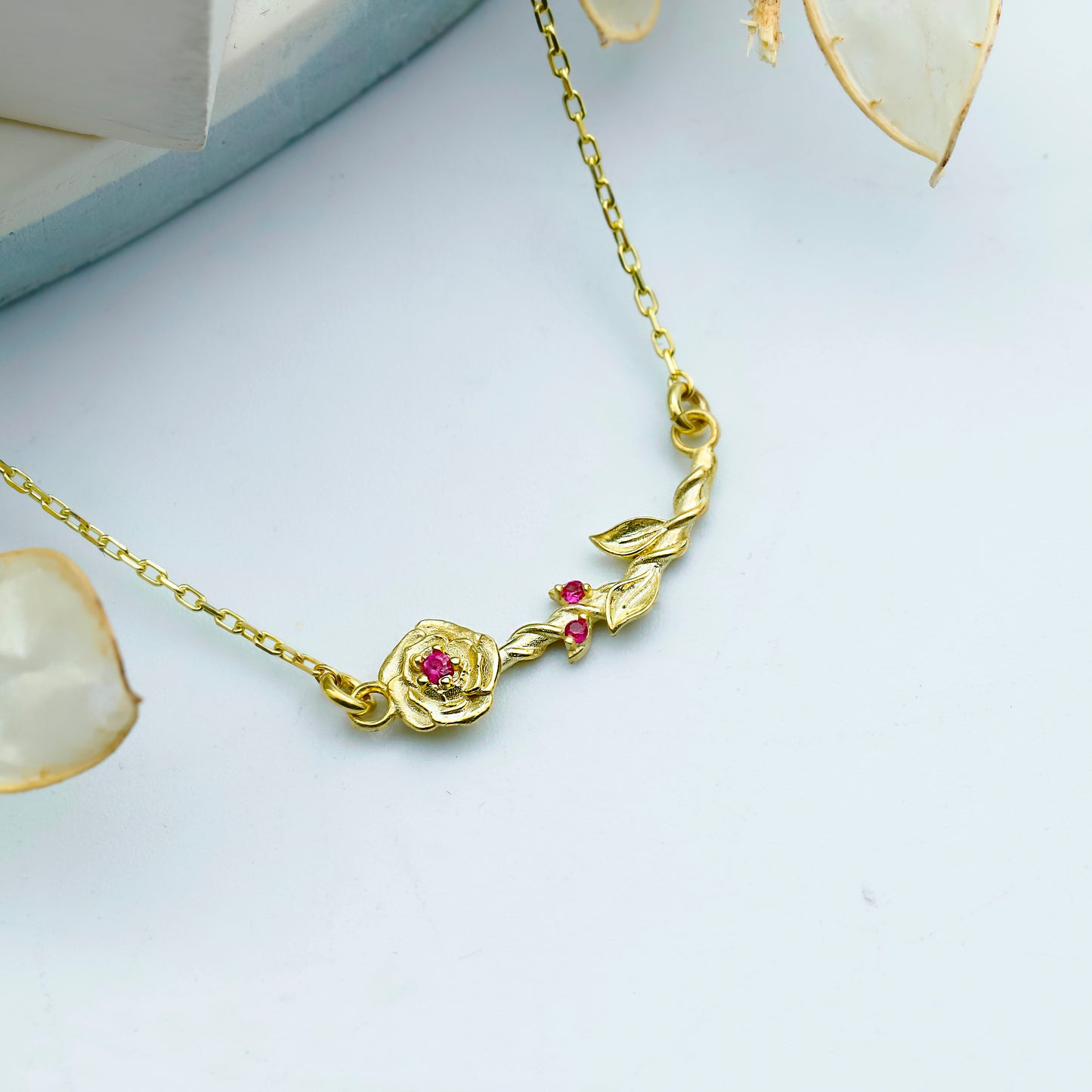 Gold necklace with a rose design and red gemstones on a light gray background