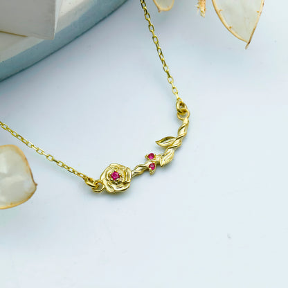 Gold necklace with a rose design and red gemstones on a light gray background