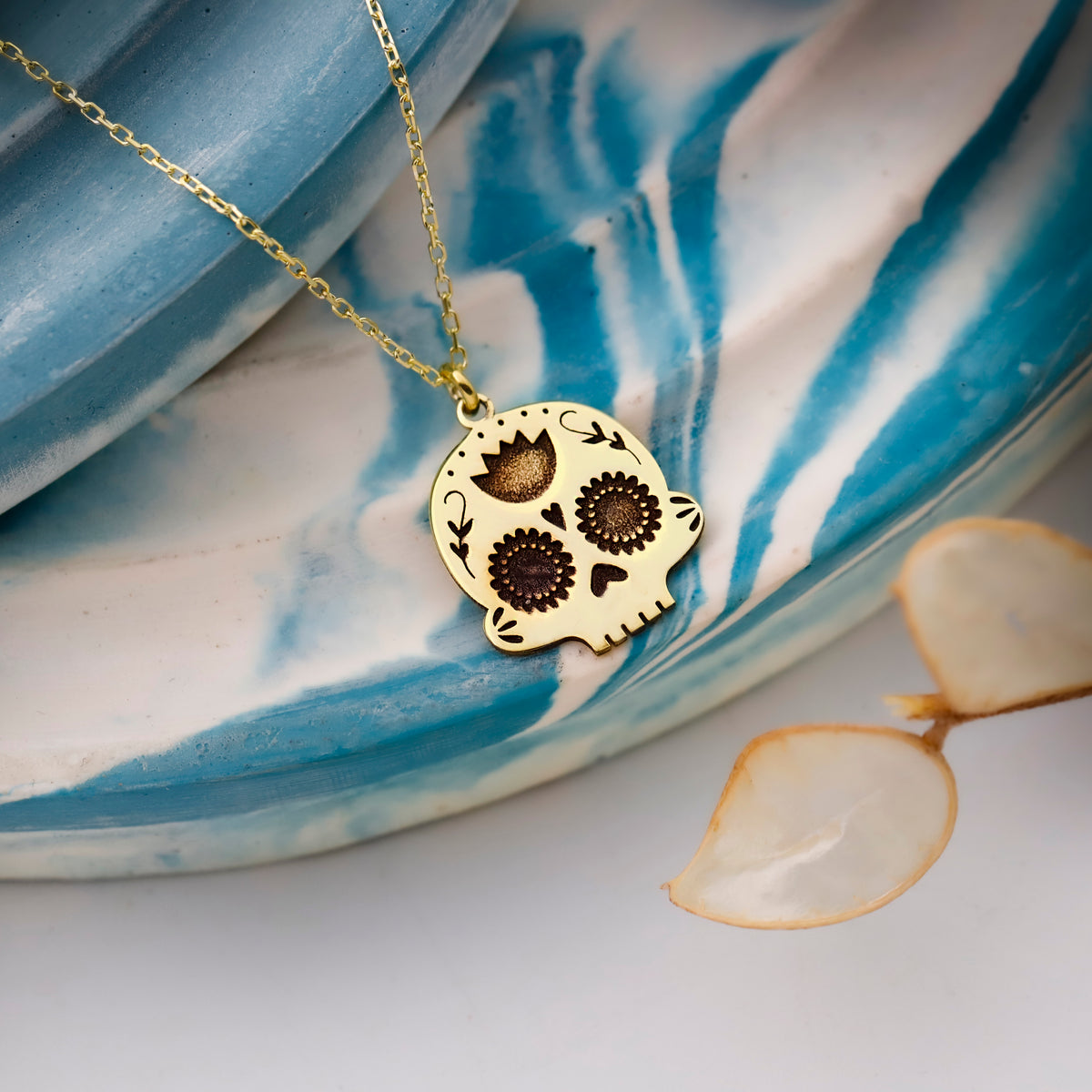 Gold skull-shaped pendant necklace on a blue and white ceramic dish