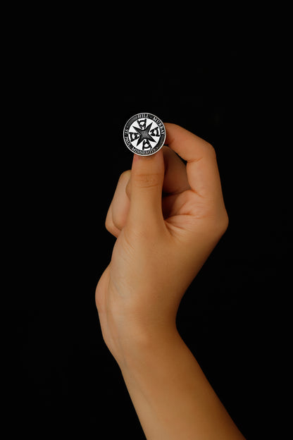 A silver brooch with an engraved university seal placed on a white fabric with a floral pattern.