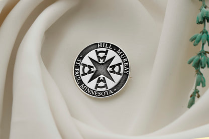 A sterling silver brooch with an engraved university seal placed on a white fabric with a floral pattern.