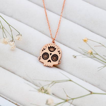 Rose gold skull-shaped pendant necklace on a white textured surface with small flowers.